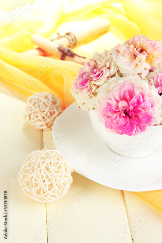 Roses in cup on wooden table on yellow cloth background