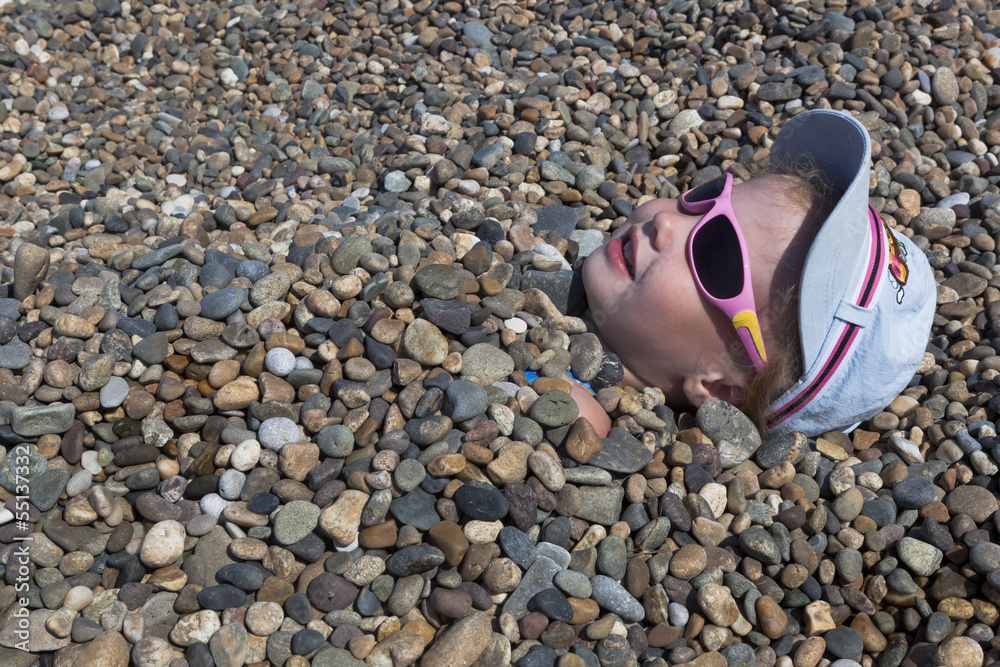 Obraz premium Девочка засыпанная камешками на пляже