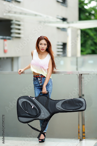 Young beautiful woman posing outdoor with her guitar gig bag