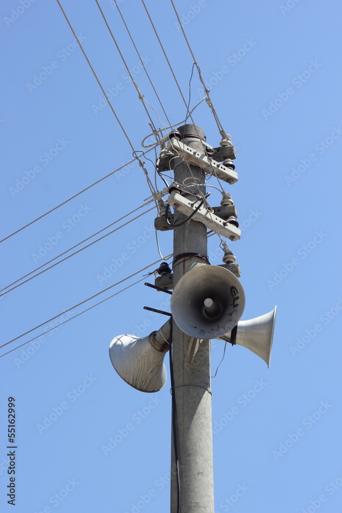 Telegraph poles with speakers and cables against a blue sky Telegraph poles with speakers and cables against a blue sky