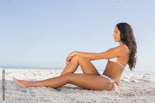 Thoughtful attractive brunette in white bikini posing while sitt