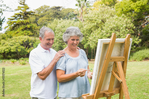 Cheerful retired woman painting on canvas with husband