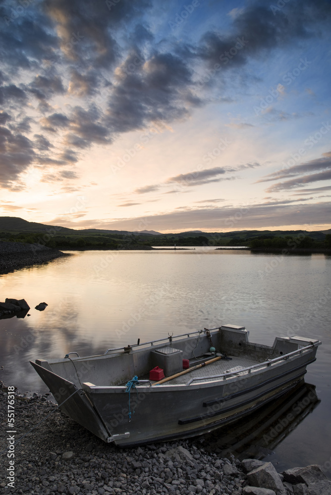 Beautiful moody sunrise over calm lake with boat on shore
