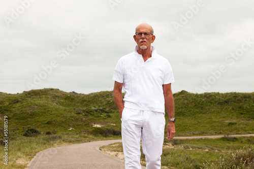 Retired senior man with beard and glasses walking outdoors in gr