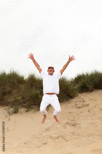 Jumping happy retired man with beard and sunglasses in grass dun