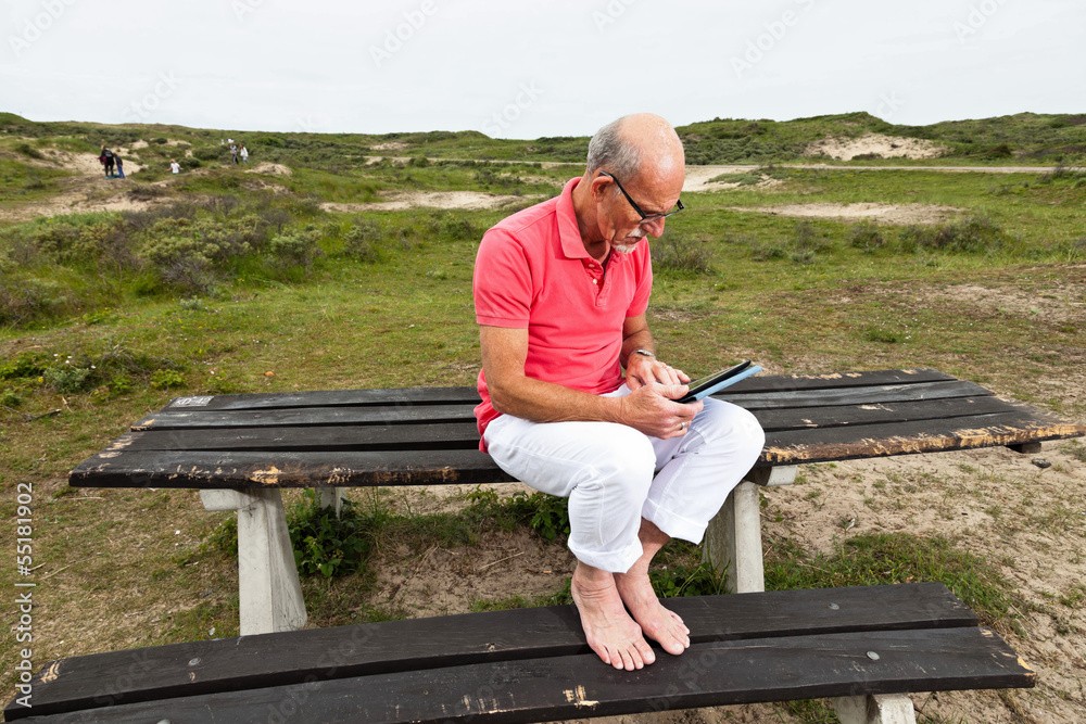 Fototapeta premium Retired senior man resting and using his tablet at table in park
