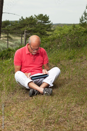 Senior retired man sitting with tablet outdoors in meadow. Scott