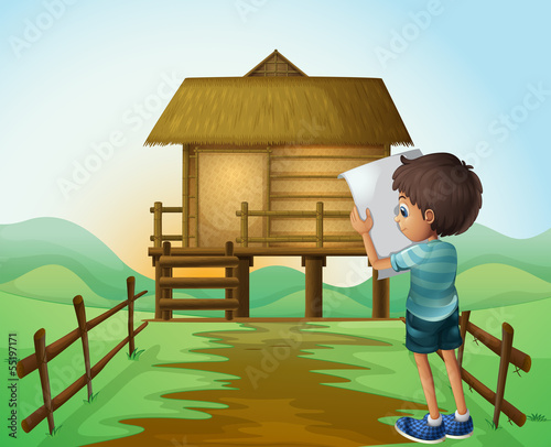 A boy with a paper in front of the nipa hut