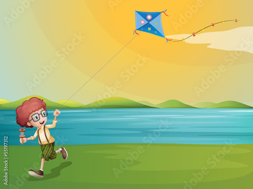 A young boy playing with his kite at the riverbank