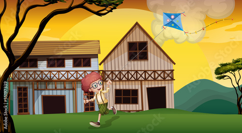A boy playing with his kite in front of the wooden barnhouses