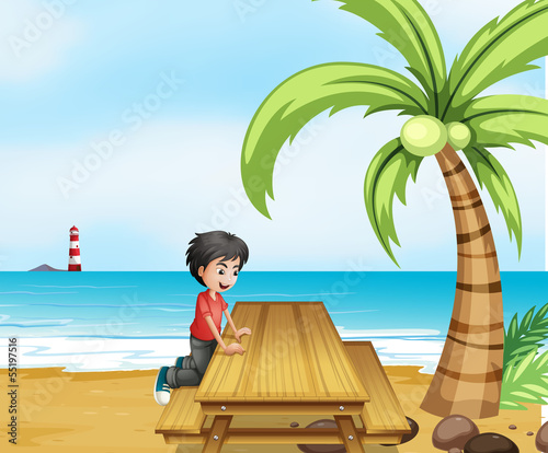 A boy at the beach with a wooden table near the coconut tree