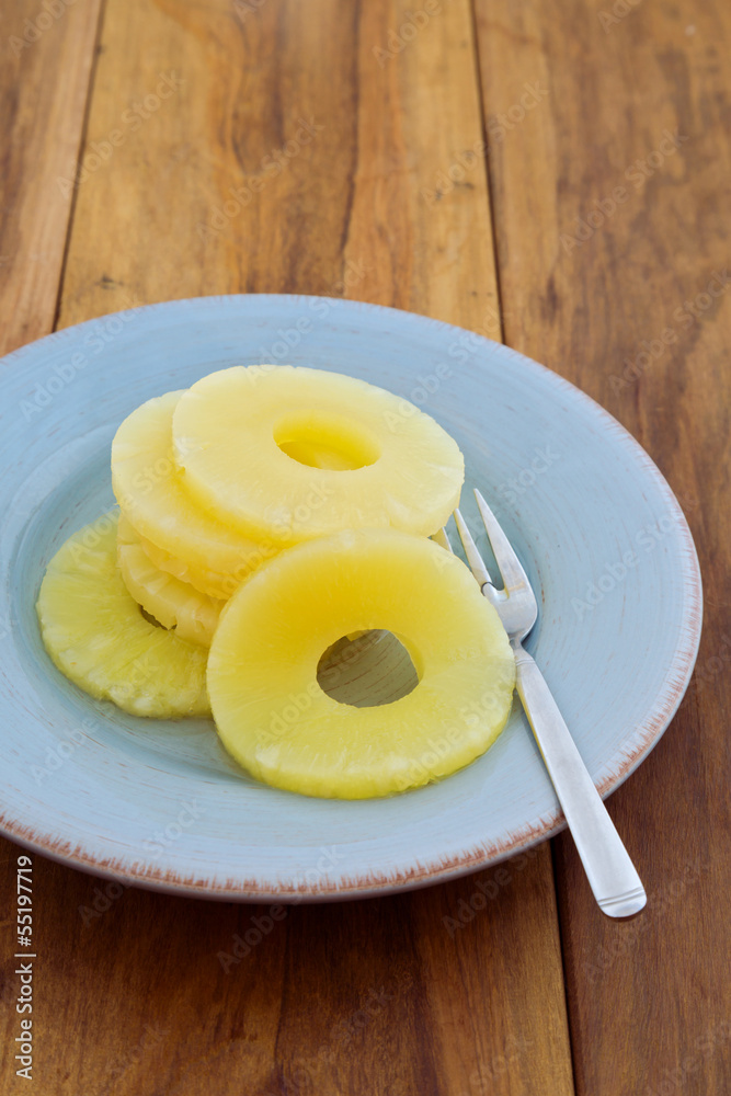 Pineapple in syrup on plate over wooden background Pineapple in syrup on plate over wooden background