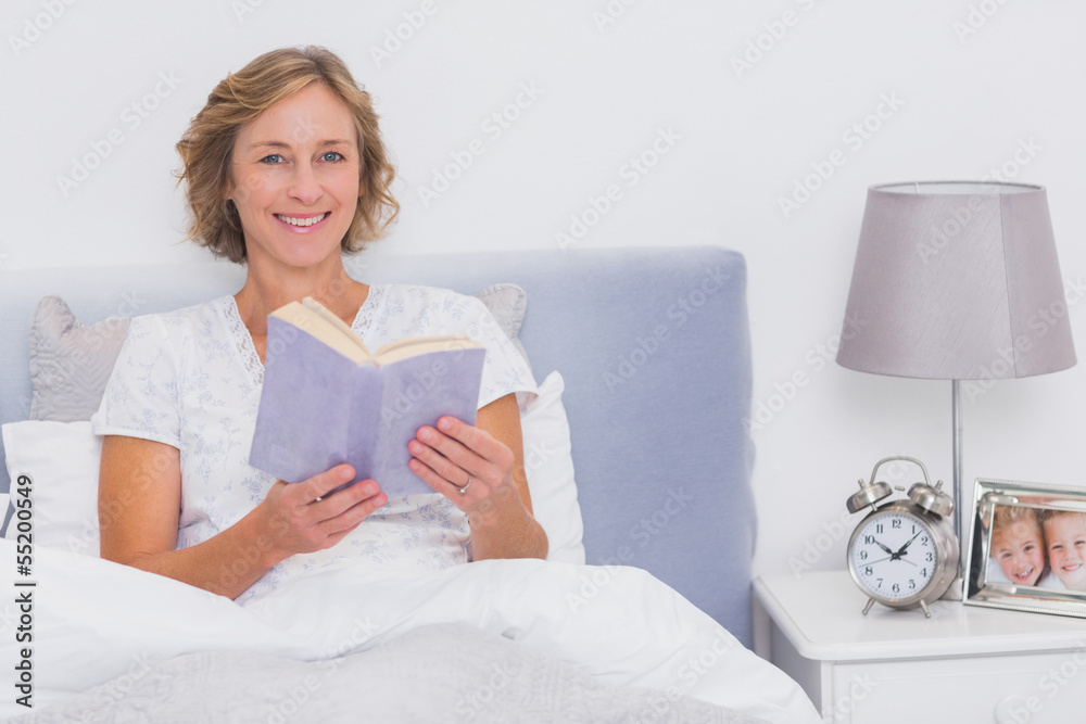 Relaxed blonde woman sitting in bed holding book Relaxed blonde woman sitting in bed holding book