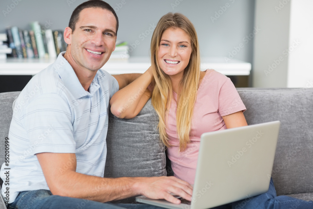 Smiling couple sitting using laptop on the couch together