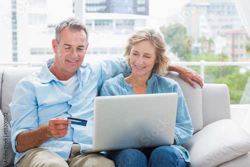 Smiling couple sitting on their couch using the laptop to buy on