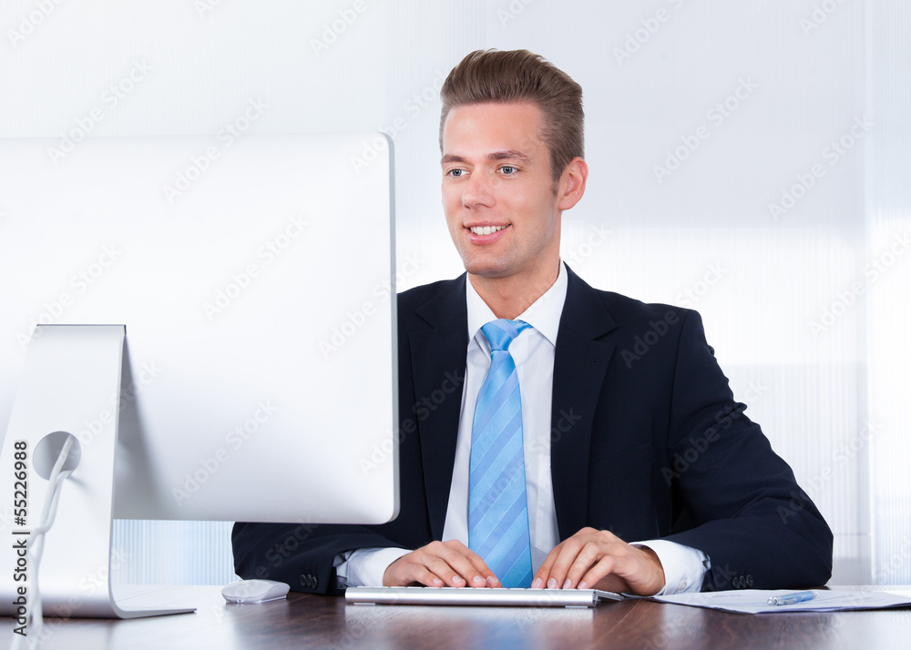 Happy Young Businessman Using Computer In Office Happy Young Businessman Using Computer In Office