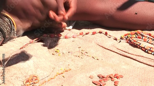 Junge Himba Frau erzeugt Schmuck auf ihrer Matte im Schatten photo