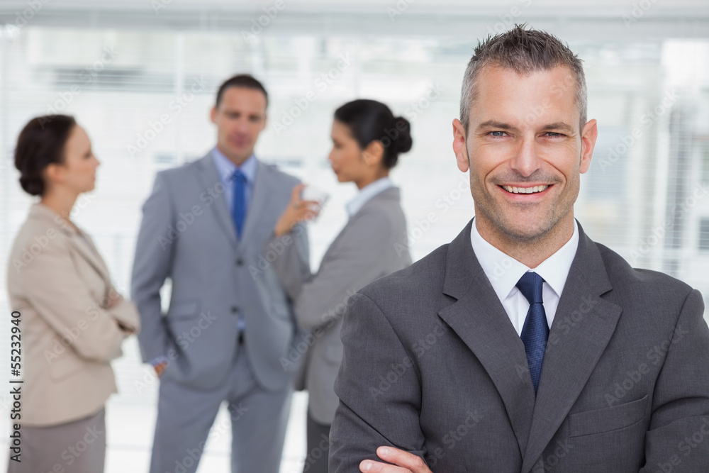 Smiling manager posing with employees in background Smiling manager posing with employees in background
