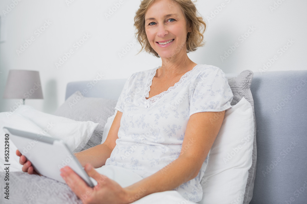 Blonde woman sitting in bed using tablet pc Blonde woman sitting in bed using tablet pc