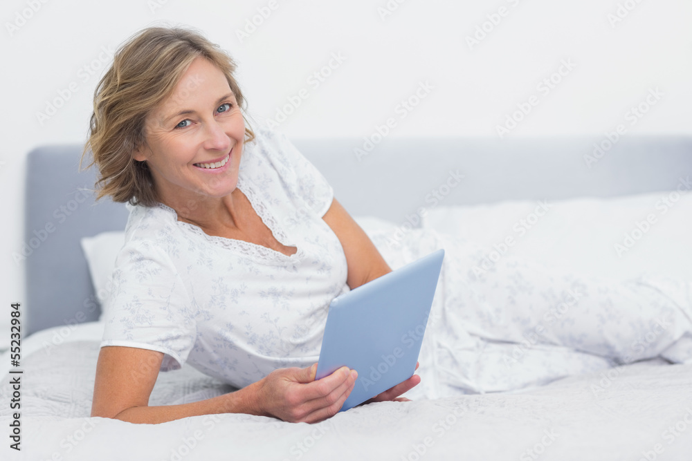 Cheerful blonde woman lying on bed using tablet pc Cheerful blonde woman lying on bed using tablet pc