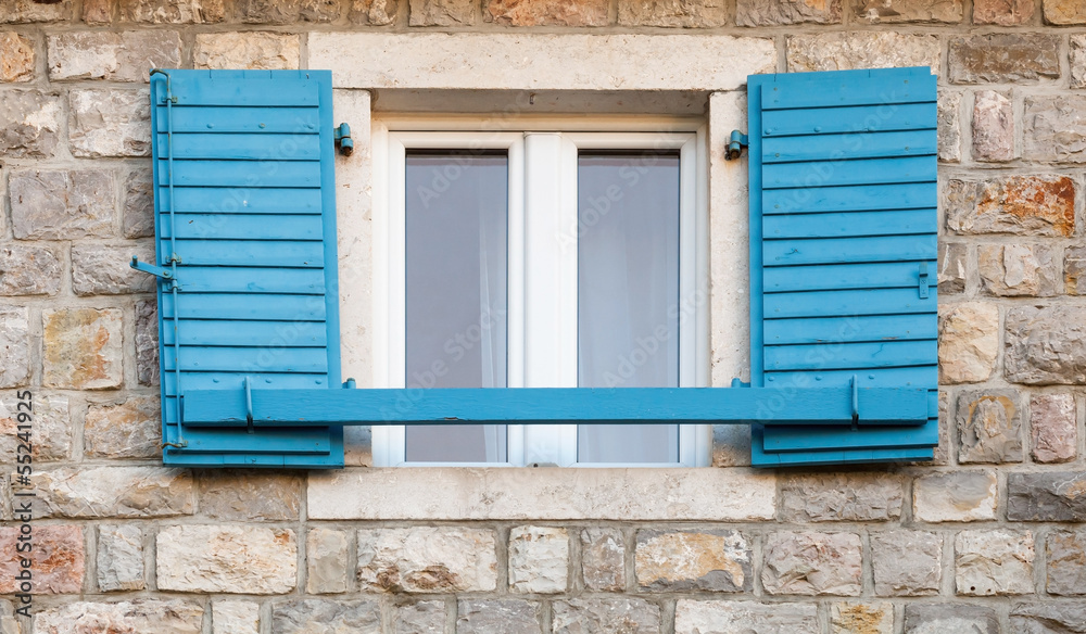 Wooden window with blue open jalousies in old gray stone wall Wooden window with blue open jalousies in old gray stone wall