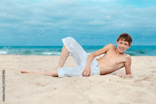 Portrait of teenage lying on sand near sea