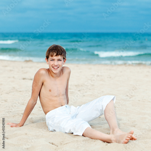 Portrait of teenage sitting on sand near sea