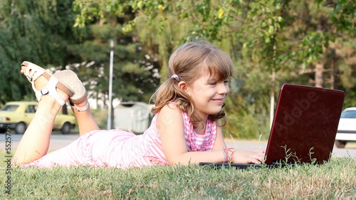 little girl lying on grass with laptop