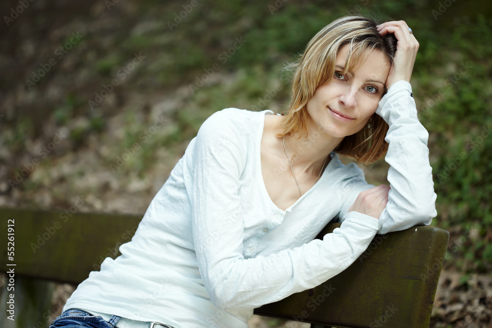 Obraz premium Portrait of smiling woman sitting on a bench in a park