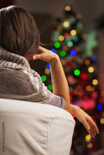 Woman sitting in armchair in front of christmas tree . rear view