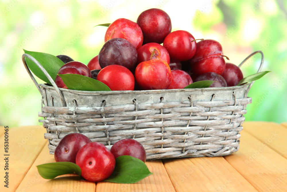 Ripe plums in basket on wooden table on natural background Ripe plums in basket on wooden table on natural background