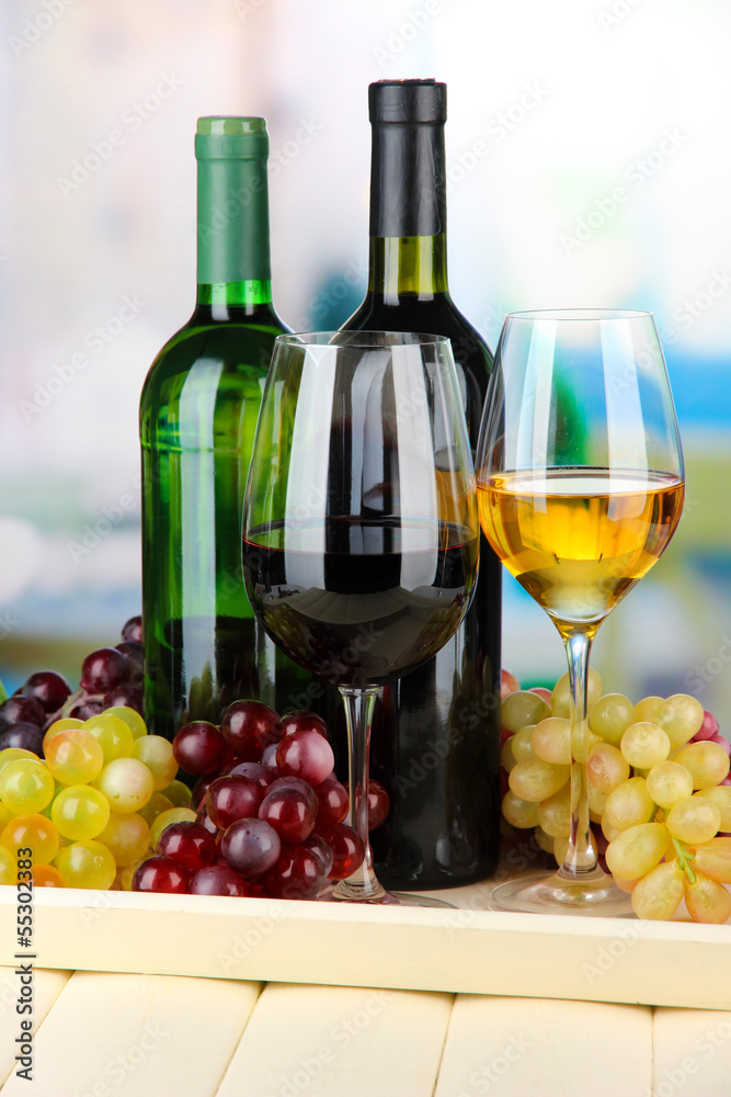 Wine bottles and glasses of wine on tray, on bright background