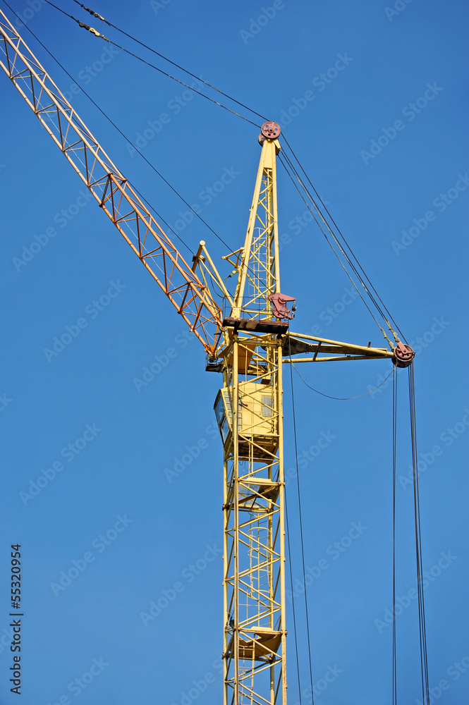 Yellow construction tower crane against blue sky