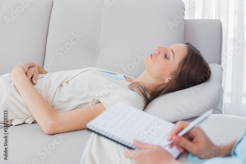 Pensive woman lying on the couch while psychologist writing