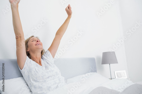 Well rested blonde woman stretching in bed and smiling