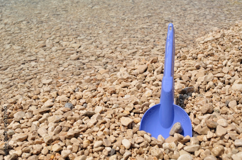Beach toys - blue shovel on the pebbly beach Beach toys - blue shovel on the pebbly beach