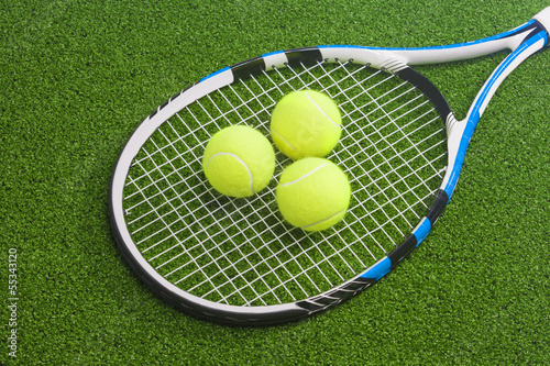 Tennis racket with three balls lies on a green lawn surface. ten