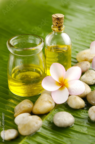 Massage oil and Plumeria flower and stones on green banana leaf