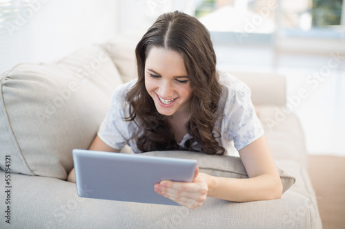 Cheerful woman lying on a cosy couch using tablet pc