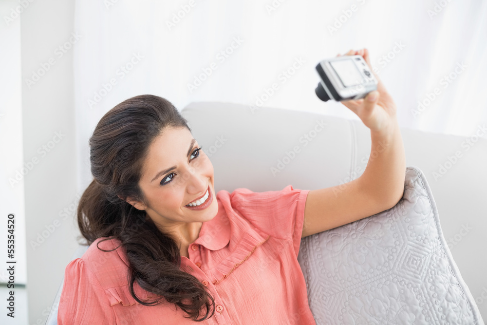 Brunette sitting on her sofa taking a picture of herself Brunette sitting on her sofa taking a picture of herself