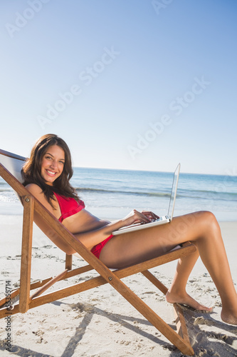 Pretty woman using her laptop while relaxing on her deck chair