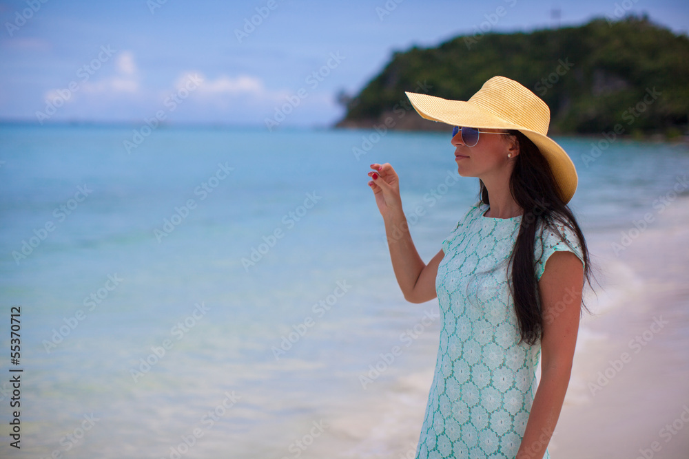 Beautiful young girl in yellow hat standing near water at beach