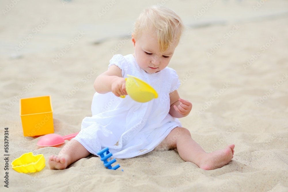Funny baby girl plays with toys sitting in sand on playground Funny baby girl plays with toys sitting in sand on playground