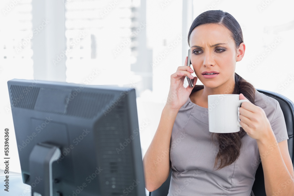 Frowning businesswoman holding coffee and answering phone Frowning businesswoman holding coffee and answering phone