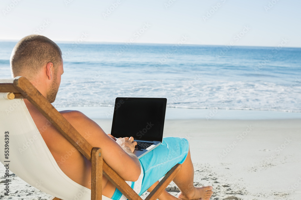 Handsome man typing on his laptop while sitting on his deck chai
