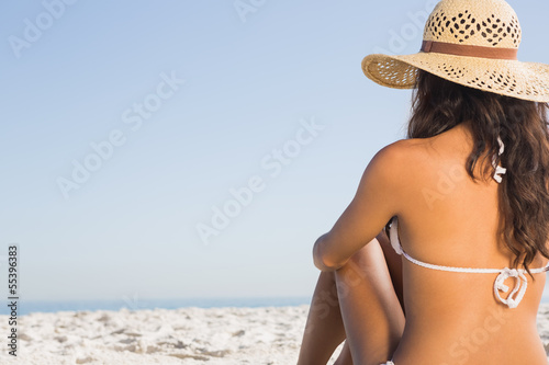 Pensive attractive brunette in white bikini sitting
