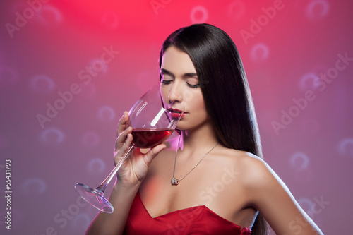 Drinking red wine. Beautiful young woman in red dress holding a