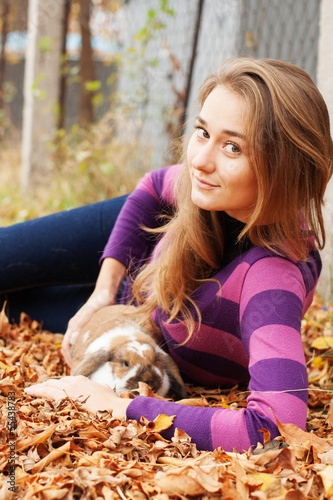 Happy girl walking in autumn park with her rabbit