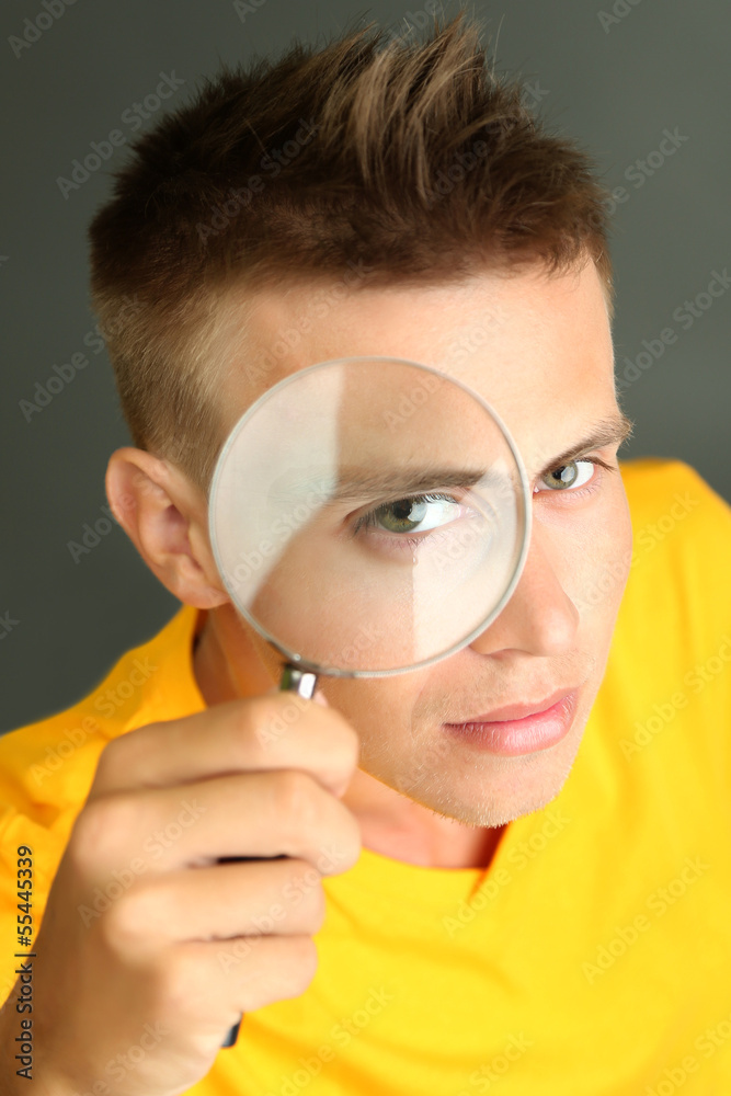 Young man looking through magnifying glass on grey background Young man looking through magnifying glass on grey background