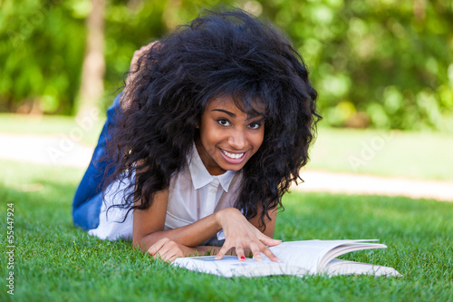 Young student girl reading a book in the school park - African p